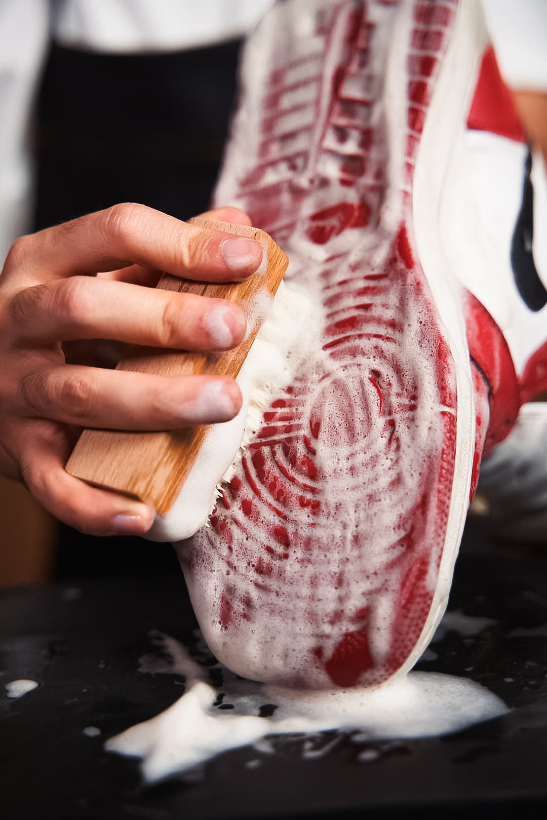 Cepillo aplicando espuma sobre una zapatilla sucia